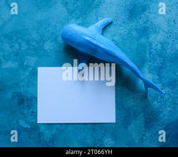 baleine jouet avec une carte de papier vierge avec un fond aquarelle bleu Banque D'Images