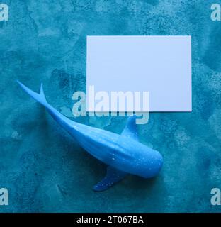 baleine jouet avec une carte de papier vierge avec un fond aquarelle bleu Banque D'Images