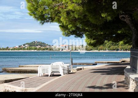 Vodice, Croatie - 24 septembre 2023 : promenade vide avec des pins près de la plage de bord de mer et des chaises longues empilées, à la fin de la saison Banque D'Images