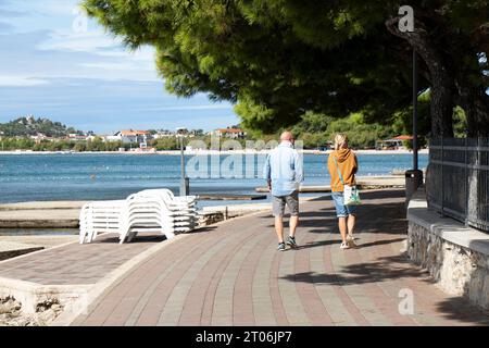 Vodice, Croatie - 24 septembre 2023 : les gens marchent sur la promenade près de la plage de bord de mer hors saison, par derrière Banque D'Images