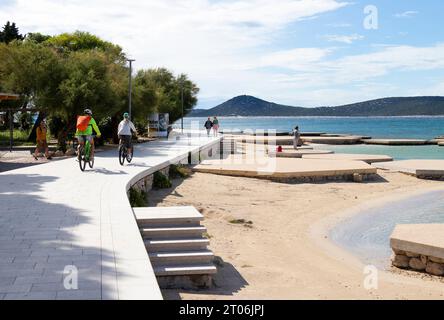 Vodice, Croatie - 24 septembre 2023 : les gens marchent et font du vélo sur la promenade près de la plage de bord de mer au coucher du soleil hors saison Banque D'Images