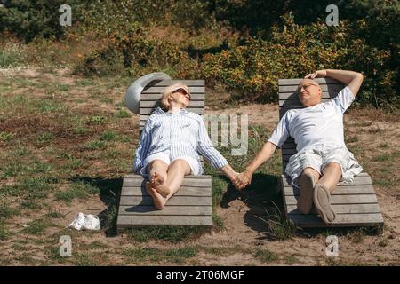 Un couple de personnes âgées mignonnes s'allongent sur des transats se tenant la main, se prélassant au soleil. Banque D'Images