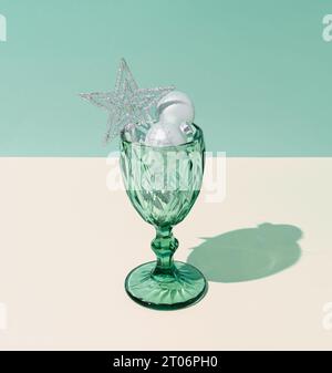 Boules de Noël décoration cocktail dans un verre à vin sur fond vert pastel et crème. Concept de fête du nouvel an ou de la veille de Noël. Banque D'Images