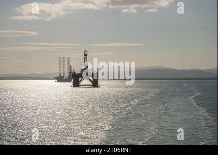 Plate-forme pétrolière et navire d'installation d'éoliennes offshore dans la baie d'Invergordon au coucher du soleil, vue de la distance, en Écosse Banque D'Images