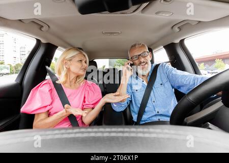 Femme âgée en colère criant pendant que le conducteur de voiture parle au téléphone Banque D'Images