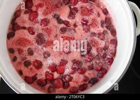 étape de fabrication de confiture de fraises maison. Les baies mûres bouillent avec le sucre dans une casserole sur la plaque de cuisson. Heure d'été pour la mise en conserve de confiture de baies. vue de dessus Banque D'Images