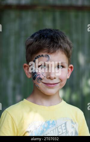 Portrait de garçon d'âge préscolaire avec scorpion peint sur son visage. Peinture faciale festive. Heureux enfant aux yeux bruns dehors sur fond vert. Été. corps Banque D'Images