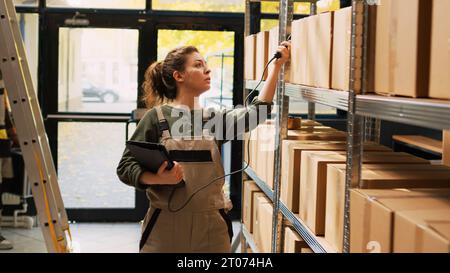 L'employé de l'entrepôt lit les codes-barres à l'aide d'un lecteur de tablette pour l'inventaire de l'entrepôt et vérifie les produits. Femme travailleuse vérifiant la logistique des stocks de marchandises, inspection d'entrepôt. Banque D'Images