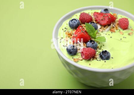 Savoureux bol de smoothie matcha servi avec des baies et des flocons d'avoine sur fond vert, gros plan avec espace pour le texte. Petit déjeuner sain Banque D'Images