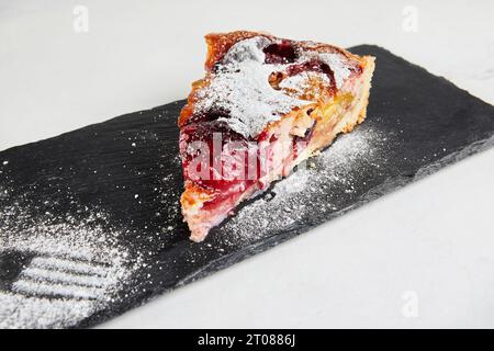 Tarte aux prunes avec kinaman saupoudrée de sucre en poudre sur pierre noire. Banque D'Images