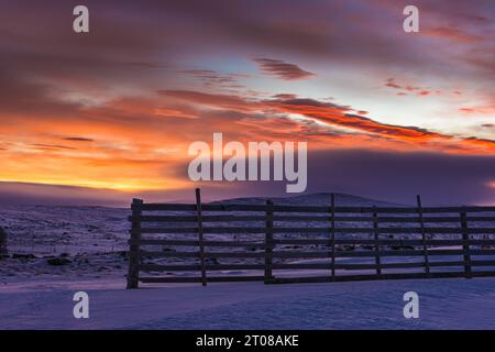Un lever de soleil hivernal serein sur des montagnes enneigées et une clôture de neige. Banque D'Images