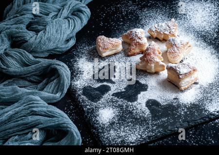 Biscuits faits maison avec du sucre en poudre sur une planche de service en ardoise avec une nappe de gaze grise sur un fond noir. Banque D'Images