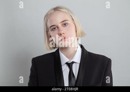 Femme blonde habillée en costume et cravate pose sur fond blanc Banque D'Images