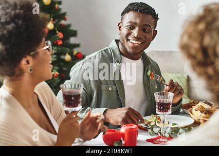 Heureux homme et femme afro-américains assis à la table de Noël appréciant la nourriture, souriant l'un à l'autre Banque D'Images