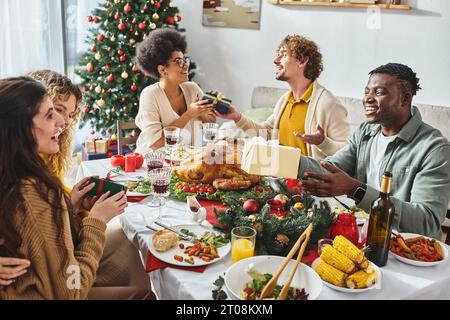 Grande famille joyeuse et multiraciale ayant beaucoup de temps pour célébrer Noël et échanger des cadeaux Banque D'Images