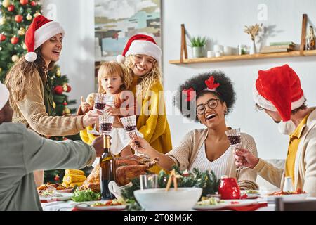 Grande famille joyeuse multiethnique clinking leurs lunettes à la table de fête portant des chapeaux de Père Noël, Noël Banque D'Images