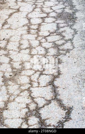 Fissures du tarmac assez fortement délimitées rendues visibles par l'infiltration d'eau de pluie dans la surface fissurée. La teinte orange provient de la terre rougeâtre dans l'eau. Banque D'Images