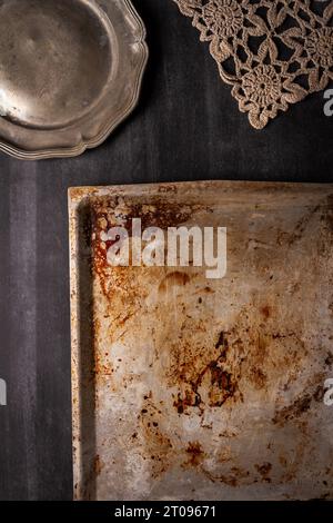 Moule plat de four usagé avec des taches brûlées et des rayures et plaque d'étain sur fond noir de tableau noir Banque D'Images