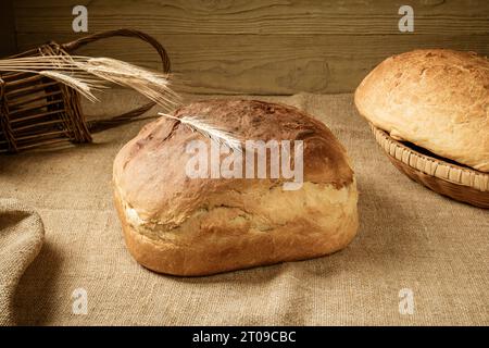 Deux miches de pain blanc maison dans un panier sur une nappe de toile de jute. A proximité se trouve un tas d'épis d'orge Banque D'Images