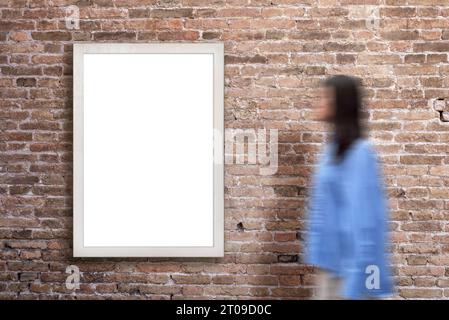 Panneau d'affichage vertical sur un mur de briques, présentant une surface vierge pour la promotion de la conception. Une femme marche à côté, créant une scène urbaine vivante pour le potentiel Banque D'Images