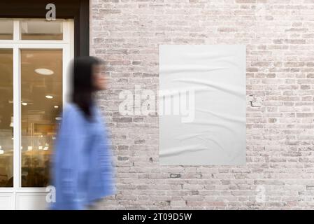 Affiche collée sur un mur de briques à côté d'une porte de magasin. Femme en mouvement marchant à côté. La scène urbaine avec mouvement dynamique pour la maquette et le design d'affiches Banque D'Images