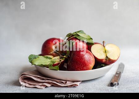 Bouquet de pommes rouges mûres dans l'assiette placée près du couteau et du tissu sur la surface grise sur fond flou Banque D'Images
