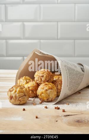 Panellets doux dans le cône de papier journal placé sur la table en bois contre le mur de carreaux blancs Banque D'Images