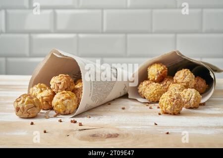 Panellets doux dans des cônes de papier journal placés sur la table en bois contre le mur de carreaux blancs Banque D'Images