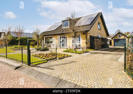 Façade de maison avec panneaux solaires sur le toit par allée pavestone et portail ouvert Banque D'Images