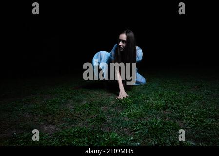 une fille effrayante dans une robe bleue est debout dans l'obscurité.une terrible femme noyée dans la forêt Banque D'Images