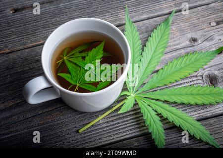 Thé au cannabis avec des feuilles de marijuana verte sur une table en bois. Tisane médicale avec du cannabis en gros plan Banque D'Images