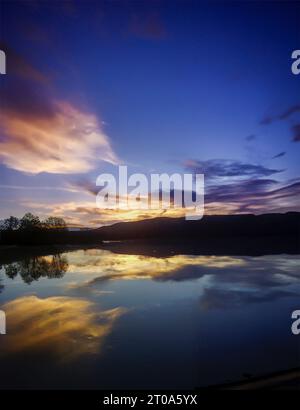 Le soleil plonge sous l'horizon, projetant les montagnes dans une silhouette majestueuse contre la toile ardente du ciel, reflétant sa myriade de couleurs Banque D'Images