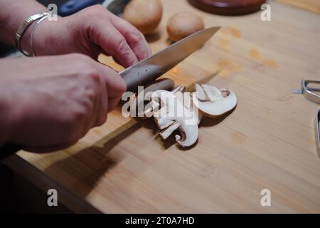 Gros plan des mains coupant des champignons frais sur le tableau de cuisine. Cuisiner des aliments sains. Banque D'Images