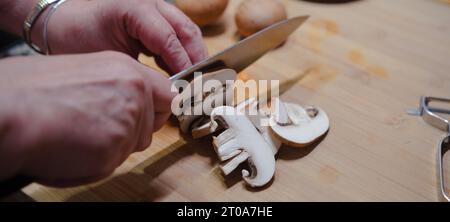 Gros plan des mains coupant des champignons frais sur le tableau de cuisine. Cuisiner des aliments sains. Banque D'Images
