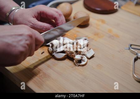 Gros plan des mains coupant des champignons frais sur le tableau de cuisine. Cuisiner des aliments sains. Banque D'Images