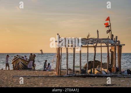 Cabane de pêcheur avec des filets de pêche sur la plage principale de Negombo au Sri Lanka avec une famille traînant autour du bateau au coucher du soleil Banque D'Images