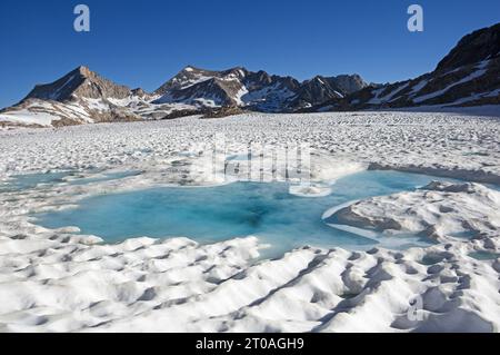 Lac gelé dans la haute Sierra commençant à fondre en juillet avec l'eau bleue dans la neige et les montagnes à l'horizon Banque D'Images