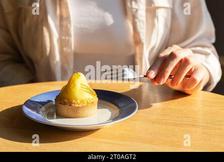 Main avec fourchette mangeant le dessert dans le café. Pâte à mousse dans la tartelette sur l'assiette Banque D'Images