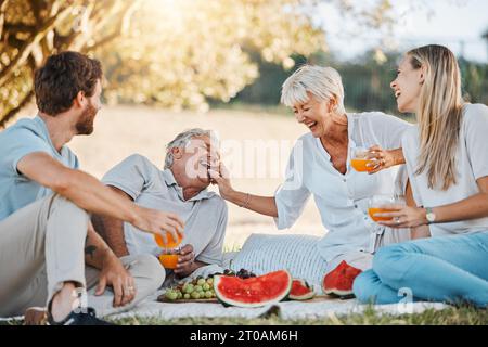 Pique-nique, famille riante et parents aînés, fille et fils s'amuser, manger des raisins et profiter de la nature en plein air, parc ou lien. Fruits de pastèque Banque D'Images