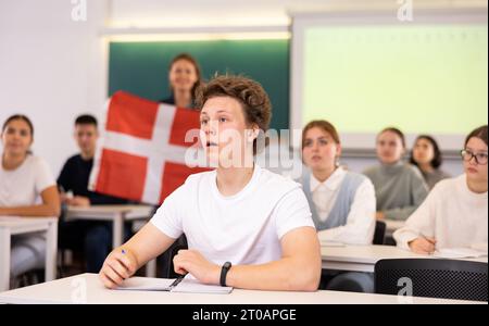 Un enseignant du secondaire parle aux élèves du Danemark et détient un drapeau du Danemark entre les mains. Banque D'Images