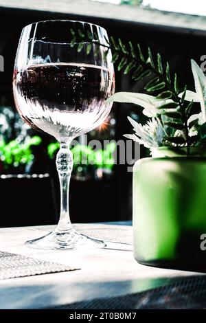 plantes vertes dans le vase vert en verre et verre de vin rose sur fond gris. Banque D'Images