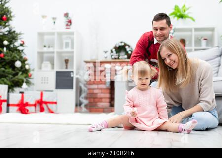 Une petite fille avec ses parents est assise dans une pièce décorée avec des ornements de Noël Banque D'Images