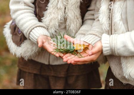 Les filles jumelles montrent les feuilles de différentes plantes qu'elles ont récoltées dans le parc d'automne. Gros plan des mains avec des feuilles. Banque D'Images