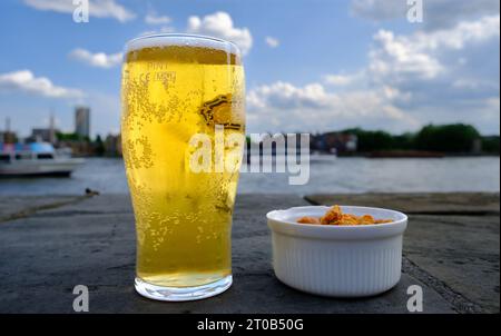 Bière et chips de pommes de terre. Verre de bière blonde avec peu de mousse. Chips dans un bol blanc bon pour snack dans un pub en plein air sur le bord de la rivière de la Tamise in Banque D'Images