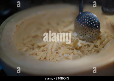 Pasta aus einem Parmesanlaib, Food, Deutschland, Rhénanie-Palatinat, 02.10.2023, das Bild zeigt eine Küchenszene, die eine kulinarische Tätigkeit darstellt. Der zentrale Fokus liegt auf einem Parmesanlaib mit Pasta, die mit einem Metalllöffel umgerührt wird. *** Pâtes à partir d'un pain de parmesan, alimentation, Allemagne, Rhénanie-Palatinat, 02 10 2023, l'image montre une scène de cuisine représentant une activité culinaire. l'accent est mis sur une miche de parmesan avec des pâtes agitées avec une cuillère en métal Credit : Imago/Alamy Live News Banque D'Images