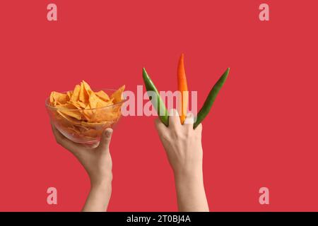 Mains femelles tenant nachos et piments forts sur fond rouge Banque D'Images