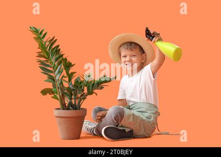 Mignon petit jardinier avec flacon pulvérisateur et plante assis sur fond orange Banque D'Images