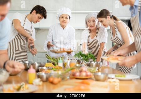 Chef en uniforme enseigne aux étudiants de cours de cuisine comment nettoyer et couper le filet de saumon Banque D'Images