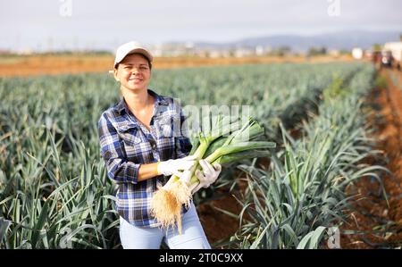Horticulteur féminin réussi avec des poireaux dans les mains debout sur le terrain Banque D'Images
