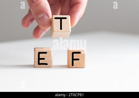 Une main masculine ajoutant la lettre T pour faire le Word ETF avec des cubes en bois sur fond rose Banque D'Images